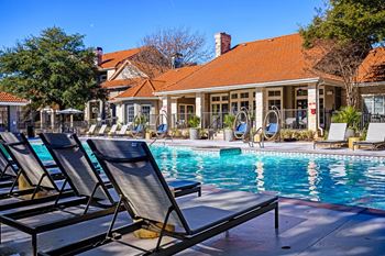 A swimming pool with lounge chairs in front of a pool house